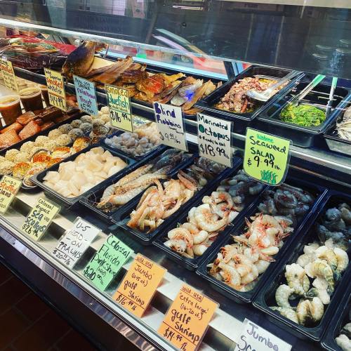 A seafood display featuring various fish, shrimp, octopus, and salads, with price tags on each item.