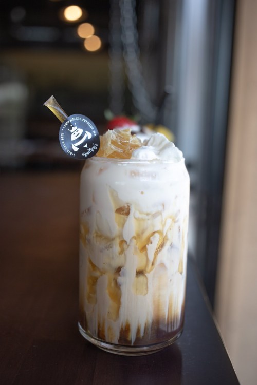 A tall glass of iced coffee with cream, topped with whipped cream and a decorative straw, sitting on a wooden table.