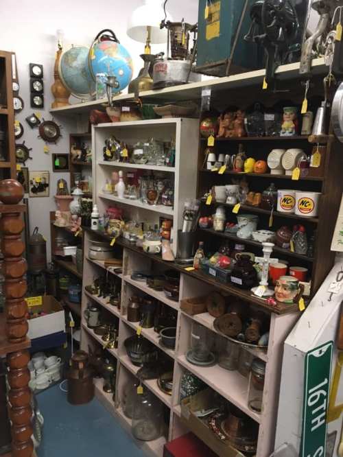 A cluttered antique shop display featuring various vintage items, glassware, and collectibles on wooden shelves.