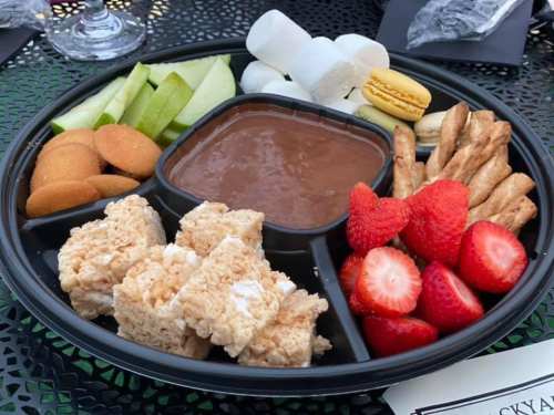 A platter with chocolate dip, strawberries, marshmallows, apple slices, cookies, and rice crispy treats.