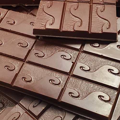 Close-up of dark chocolate bars with a wavy pattern, stacked on top of each other.