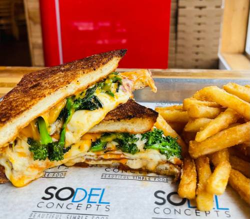 A grilled sandwich filled with melted cheese and broccoli, served with a side of crispy French fries.
