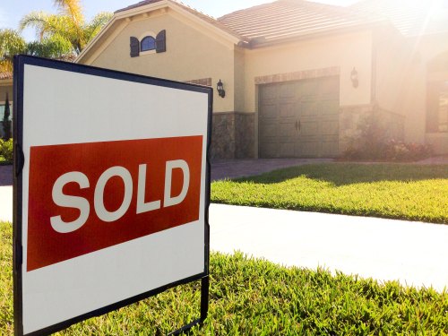 A "Sold" sign in front of a house with a well-maintained lawn and driveway, indicating the property has been sold.