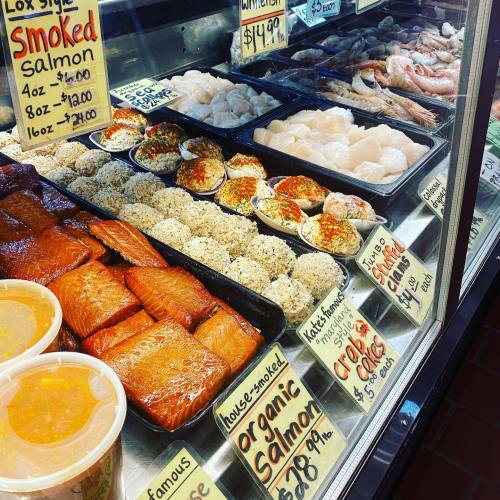 Display case filled with various seafood, including smoked salmon, scallops, and shrimp, with price tags visible.