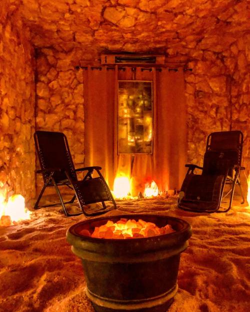A cozy, dimly lit room with stone walls, two chairs, and a bowl of crystals, creating a tranquil atmosphere.