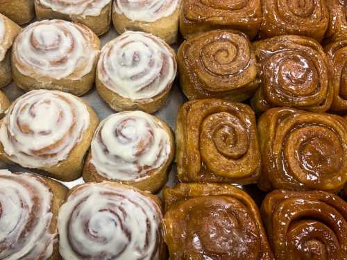 A close-up of freshly baked cinnamon rolls, some with cream cheese frosting and others glazed with caramel.