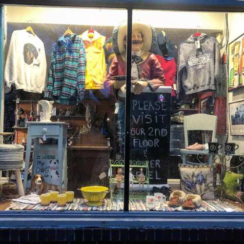 A shop window displays clothing, decor, and a large figure, inviting visitors to explore the second floor.