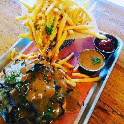A plate of fries topped with gravy and a side of dipping sauces, served on a metal tray.