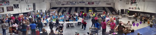 A bustling gymnasium filled with people at tables, showcasing various activities and booths during an event.