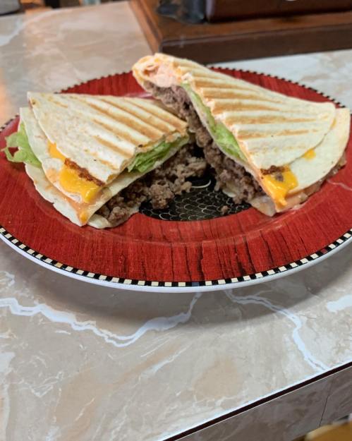 Two grilled quesadillas filled with ground beef, lettuce, and melted cheese, served on a red plate.