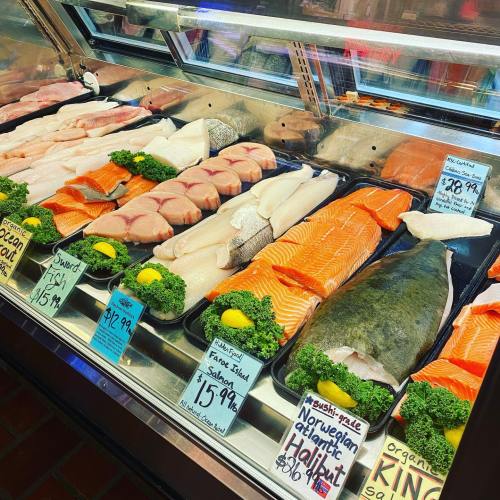 A seafood display featuring various fish fillets, including salmon and halibut, garnished with lemon and greens.