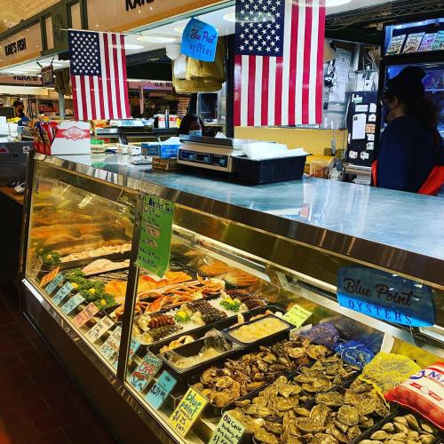 A seafood market display with fresh fish, oysters, and American flags in the background.