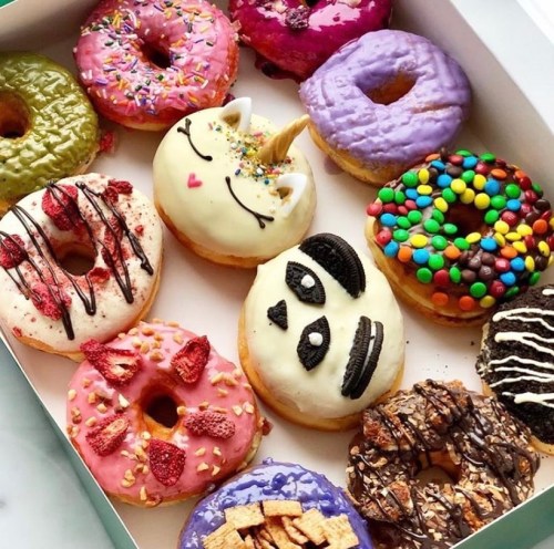 A colorful assortment of decorated donuts in a box, featuring various toppings and designs, including a unicorn and cookies.