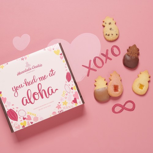 A box of cookies with a pink design, featuring pineapple-shaped cookies and the phrase "you had me at aloha."