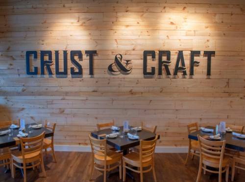 Interior of a restaurant featuring wooden walls and tables, with the words "CRUST & CRAFT" prominently displayed.