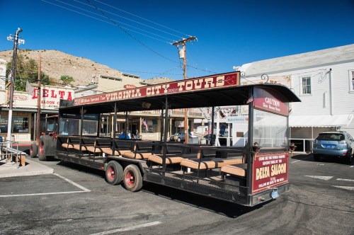 A tour bus parked in Virginia City, featuring open seating and a sign for Virginia City Tours.