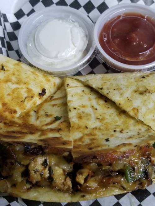 A close-up of a quesadilla cut into triangles, served with sour cream and salsa in small containers.