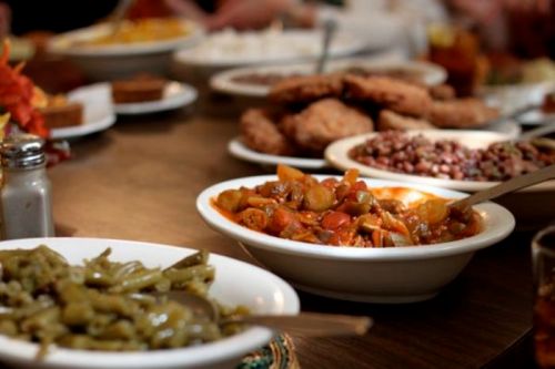 A table filled with various dishes, including green beans, mixed vegetables, fried chicken, and desserts.