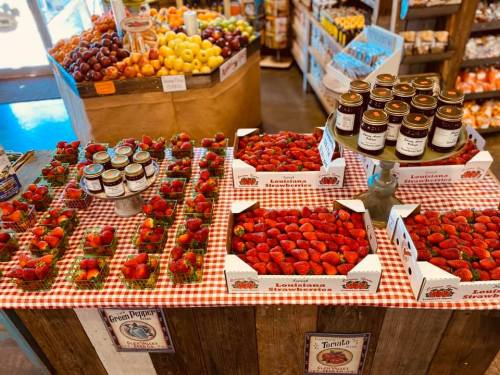 A vibrant display of fresh Louisiana strawberries and jars of preserves on a checkered tablecloth in a market.