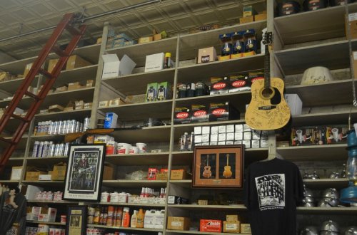 A vintage store shelf filled with various products, including guitars, cans, and boxes, with a ladder leaning against it.