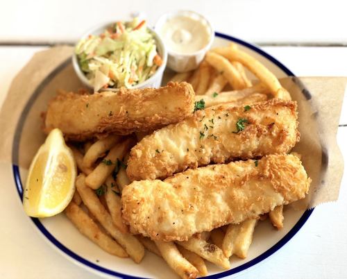 A plate of crispy fried fish fillets served with French fries, coleslaw, a lemon wedge, and dipping sauce.