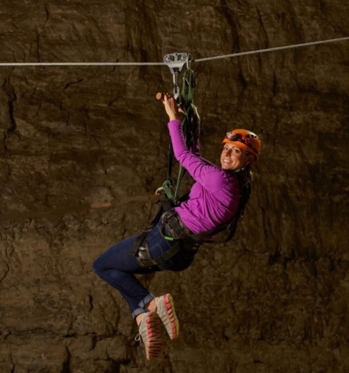 A woman in a helmet and harness zip-lining through a cave, smiling as she enjoys the adventure.