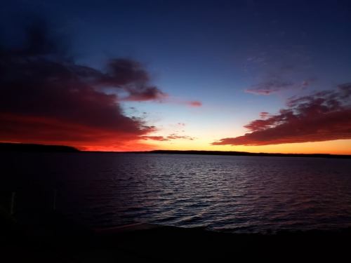 A serene sunset over a calm lake, with vibrant colors reflecting on the water and dark clouds in the sky.