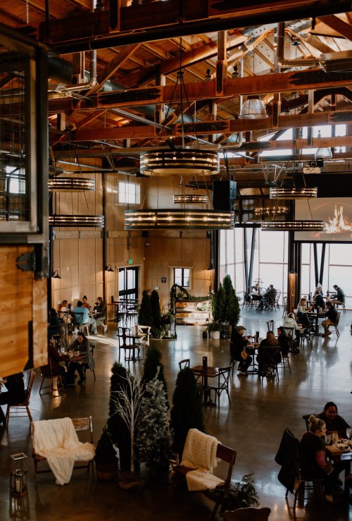 A spacious, modern restaurant with wooden beams, cozy seating, and patrons enjoying meals in a warm atmosphere.