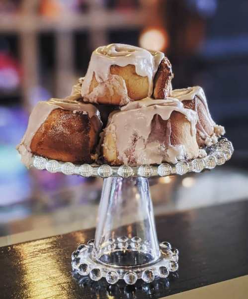 A glass cake stand displaying several frosted cinnamon rolls.