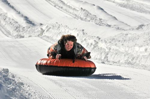 A person joyfully sledding down a snowy slope on an orange inflatable tube.