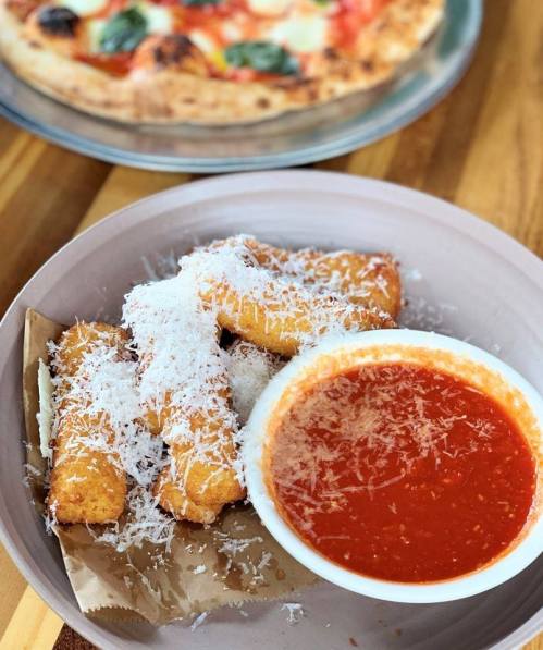 A plate of golden fried cheese sticks topped with grated cheese, served with a side of marinara sauce.
