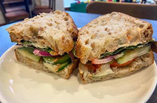 A close-up of a sandwich on whole grain bread, filled with lettuce, cucumber, tomato, and red onion, served on a plate.