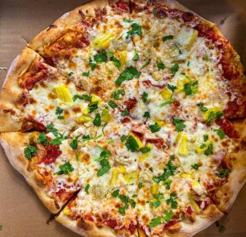 A freshly baked pizza topped with cheese, pineapple, and cilantro, served in a cardboard box.