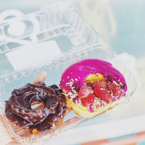 A hand holding two donuts: one chocolate-glazed and one with bright pink icing and strawberries.