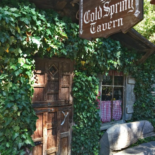 A rustic tavern entrance covered in green ivy, with a wooden sign reading "Cold Spring Tavern" above the door.