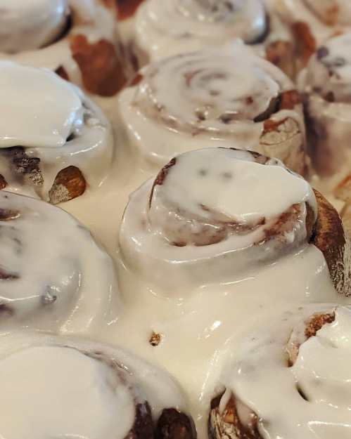 Close-up of freshly baked cinnamon rolls topped with creamy white icing.