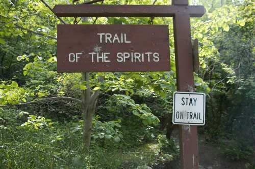 A wooden sign reads "Trail of the Spirits," with a nearby sign instructing to "Stay on Trail." Lush greenery surrounds the area.