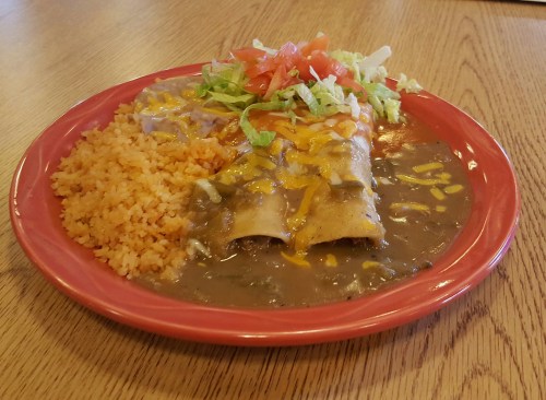 A plate of enchiladas topped with cheese, served with rice, beans, lettuce, and tomato.