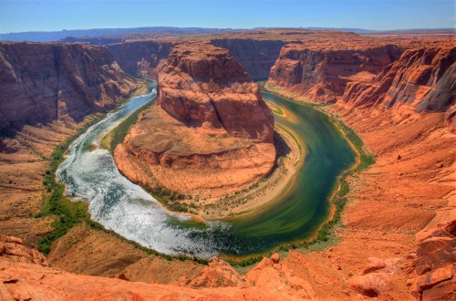 Aerial view of Horseshoe Bend, showcasing a winding river surrounded by red rock formations and clear blue skies.