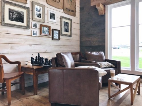 Cozy seating area with leather chairs, a wooden table, chess set, and framed photos on a rustic wall.