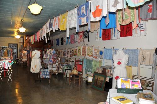 A vintage shop interior with colorful clothing and artwork displayed on walls and racks, creating a nostalgic atmosphere.