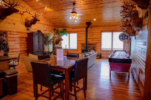 Cozy wooden interior with a dining table, seating area, and mounted animal heads on the walls.