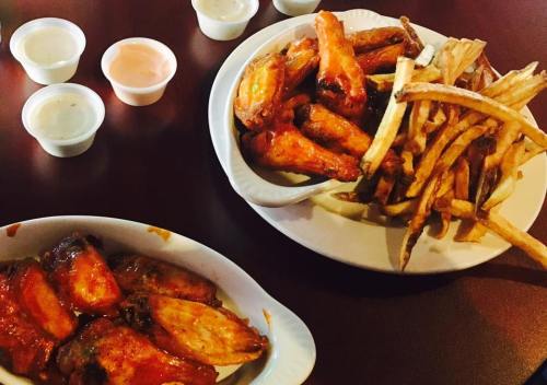A plate of crispy chicken wings with fries and dipping sauces on a wooden table.