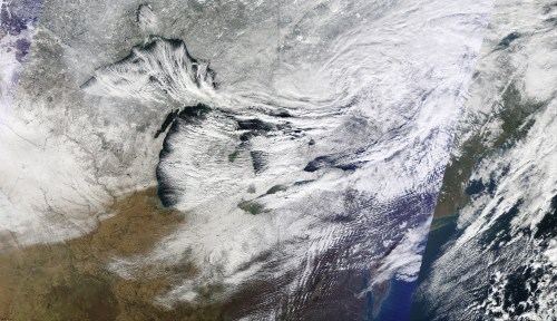 Satellite image showing the Great Lakes region, featuring snow-covered land and swirling cloud patterns.