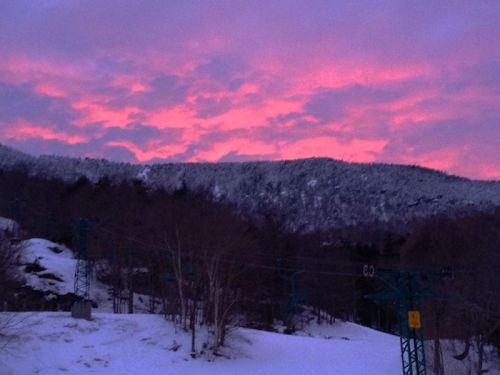 A snowy landscape with a ski lift under a vibrant pink and purple sunset sky.