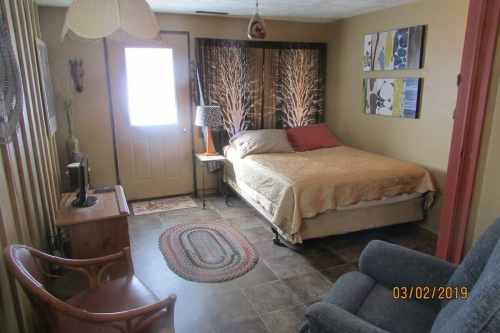 Cozy bedroom with a bed, lamp, and chair, featuring warm colors and decorative wall art.
