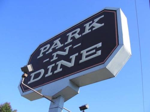 Sign for "Park-N-Dine" against a clear blue sky, featuring bold white letters on a black background.