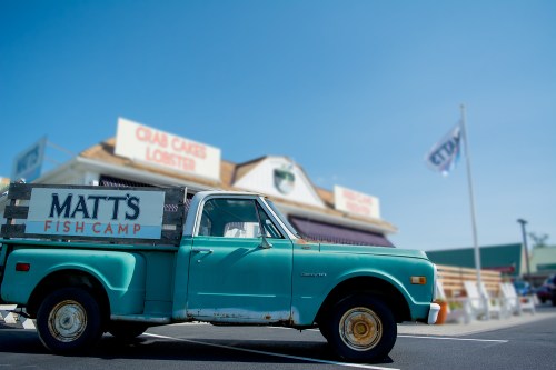 A vintage turquoise pickup truck parked in front of a seafood restaurant with a sign for "Matt's Fish Camp."