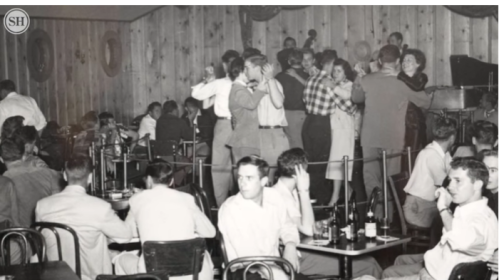 A vintage black-and-white photo of people dancing and socializing in a lively bar or dance hall.
