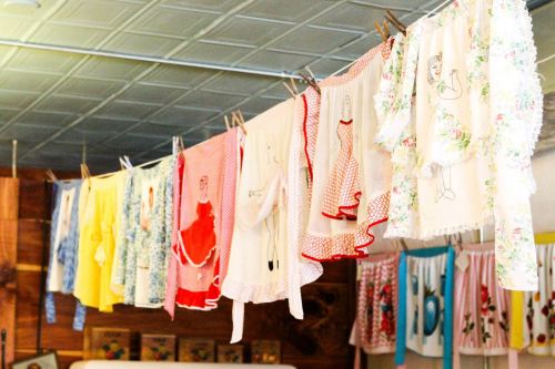 A colorful display of vintage aprons hanging on a clothesline, featuring various patterns and embroidered designs.